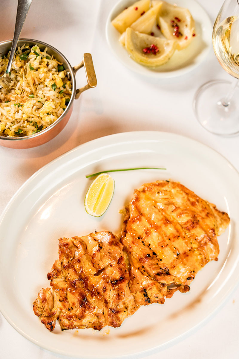 Galeto grelhado, acompanhado de arroz, alcachofras e fatia de limão, acompanhando de um refrescante vinho branco
