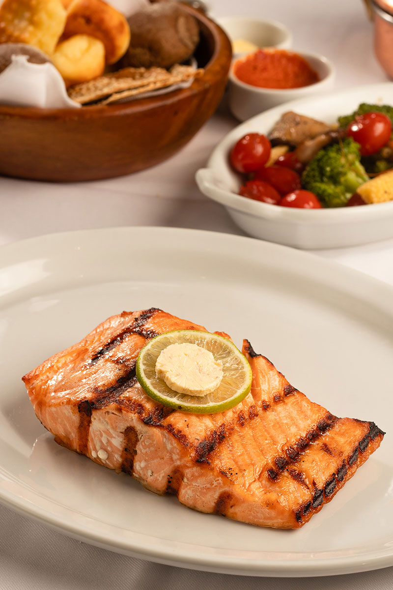 Posta de salmão grelhado com rodela de limão, porção de legumes grelhados e cesto de pães